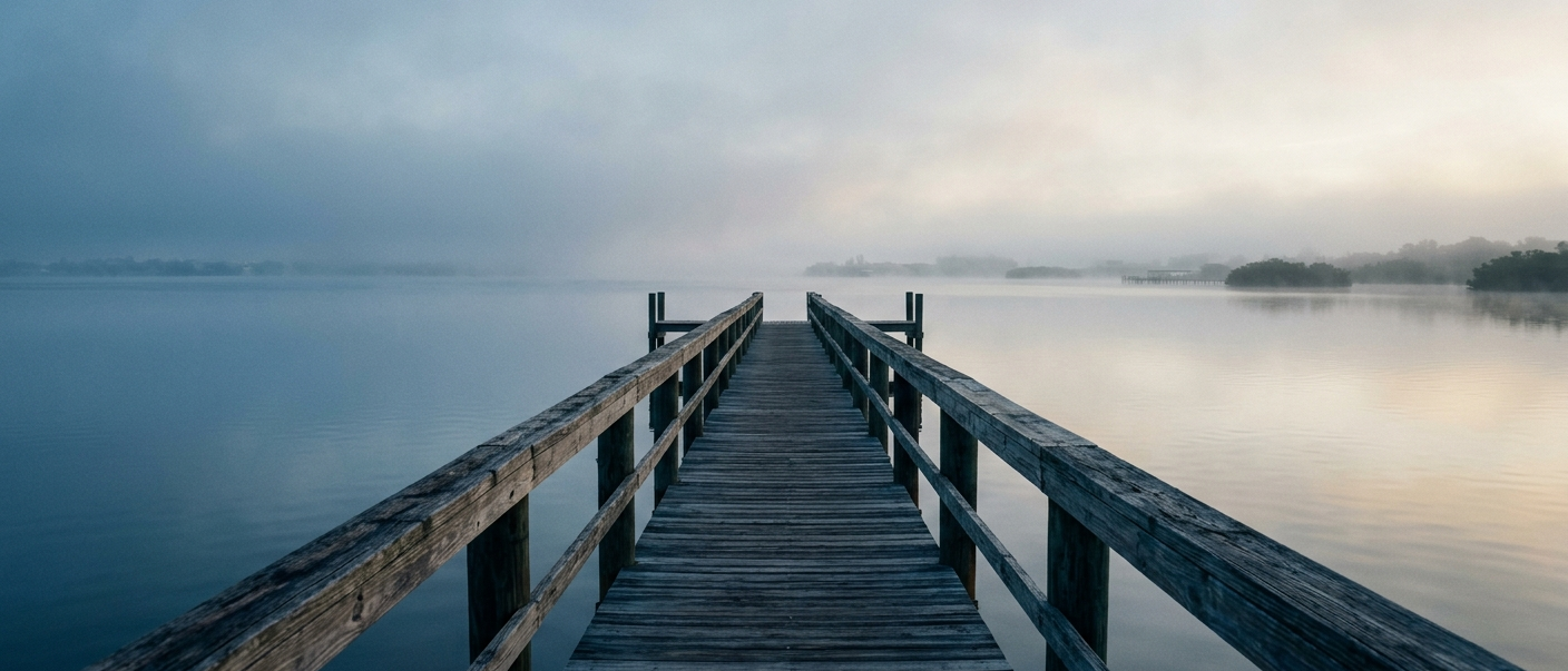 A long weathered wooden dock reaching into calm, misty Tampa Bay at early morning